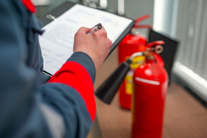 A man holds a clipboard and looks to be assessing fire extinguishers.