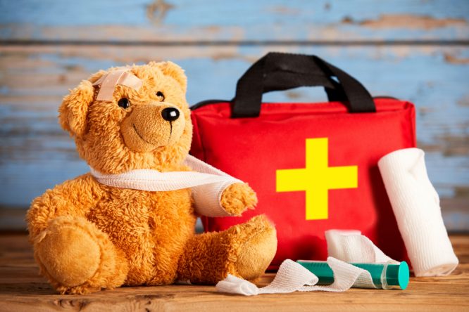 A teddy bear sat next to a first aid bag.
