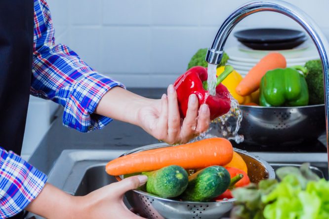 A person washes vegetables in a sink.