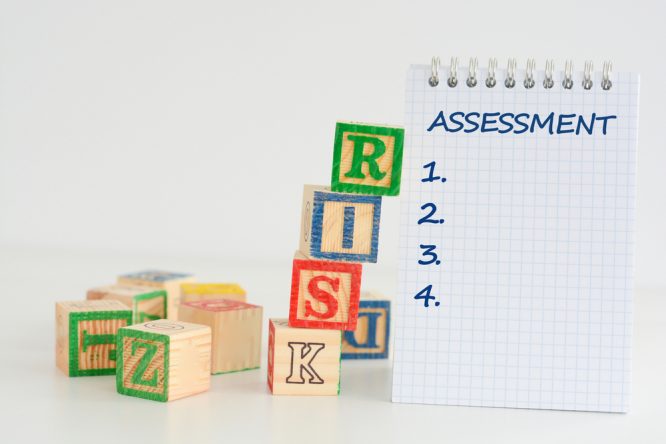 Children's letter blocks say RISK with a notepad saying Assessment with numbers 1 to 4 on it.